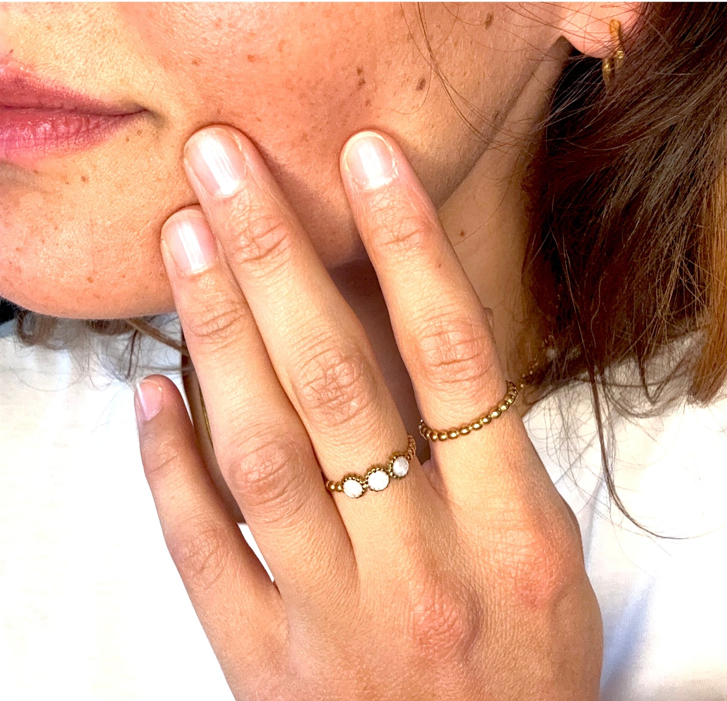 Frau trägt zwei goldene Ringe an der Hand – filigrane Designs mit weißen Steinen und Kugelstruktur.